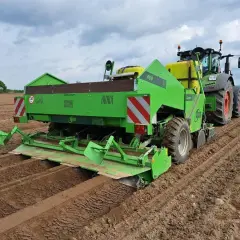 Zielona sadzarka ziemniaków pracuje na polu, tworząc rzędy do sadzenia.