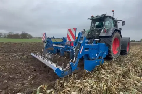 Ciągnik z agregatem uprawowym wykonuje uprawę bezorkową na polu po kukurydzy.
