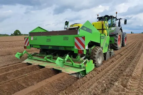 Zielona sadzarka ziemniaków pracuje na polu, tworząc rzędy do sadzenia.