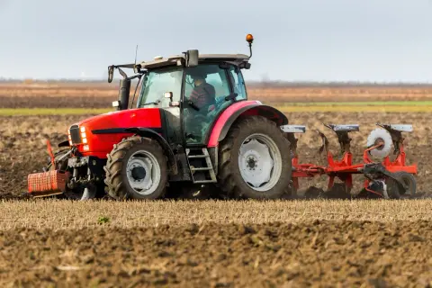 Czerwony traktor z pługiem orze pole. Rolnik przygotowuje ziemię, kiedy orka zimowa jest w pełni.