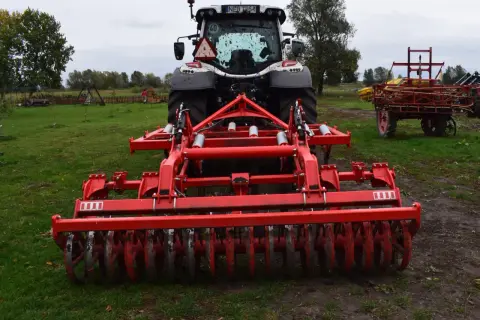 Czerwony agregat uprawowy podłączony do traktora, gotowy do siewu traw jednorocznych dla bydła.