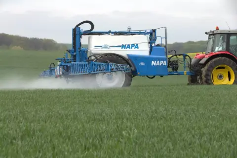Traktor z opryskiwaczem NAPA na polu zboża, aplikujący mikroelementy dla zdrowego wzrostu roślin.